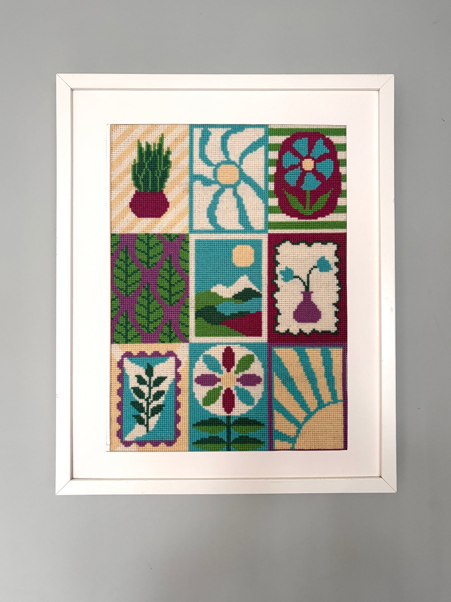 Completed Grid and Bloom counted cross stitch displayed in white frame, featuring bold floral and botanical patterns in a turquoise, greem, yelliw and dusky pink.