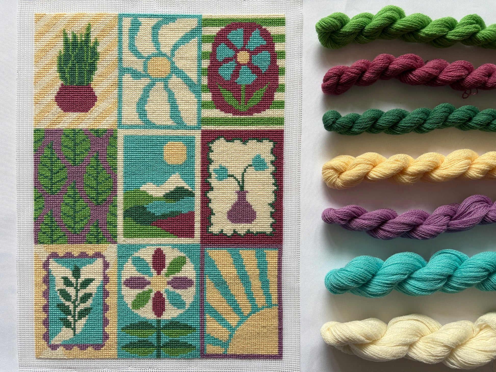 Completed Grid and Bloom Cross stitch with wool samples on a white background